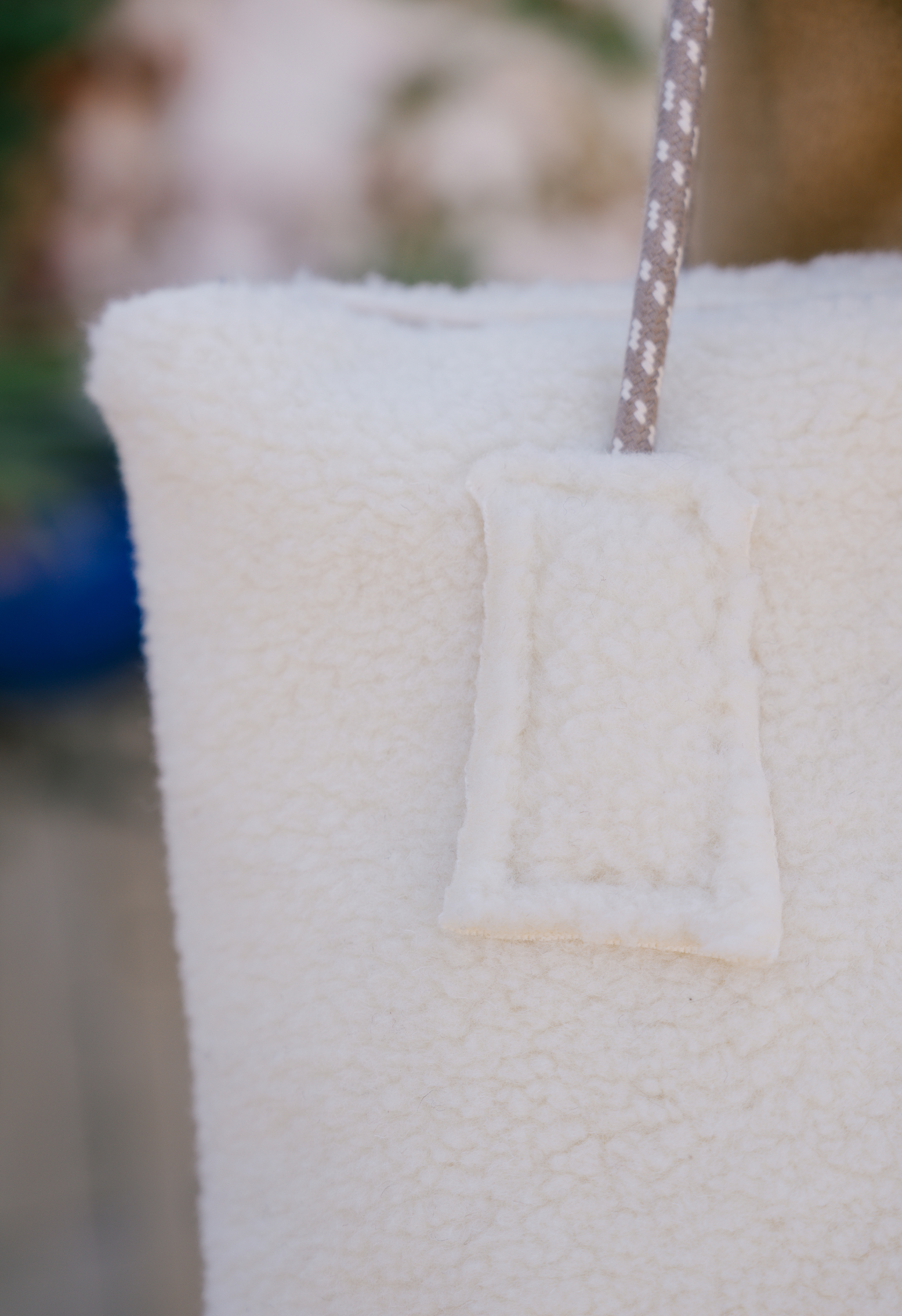 Sac en tissu crème avec une anse en corde texturée. Le sac présente une texture douce et bouclée avec une attache rectangulaire.