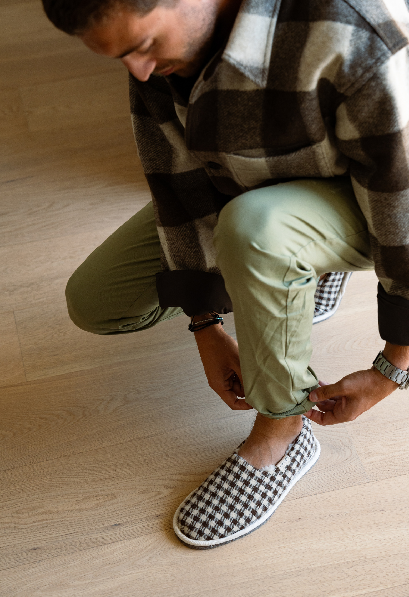 Homme ajustant le bas de son pantalon kaki tout en portant des chaussons à carreaux marron et blanc.