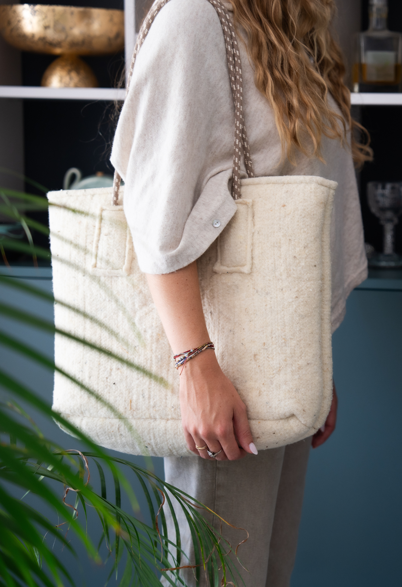 Femme tenant un sac en laine blanc texturé avec une poignée en corde beige. Elle porte un bracelet et une tenue assortie.