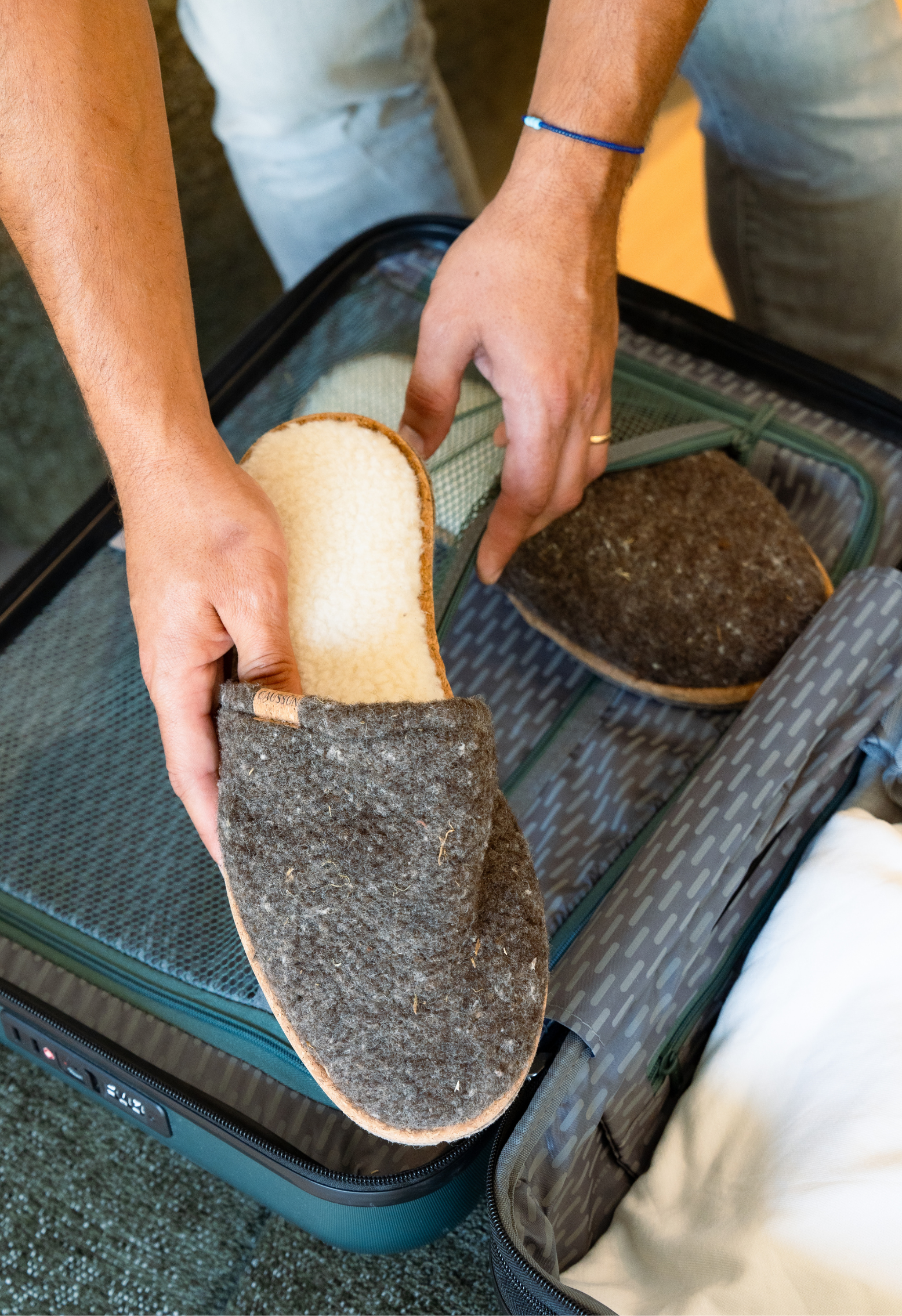 Un homme range des chaussons chauds en laine dans une valise de voyage.