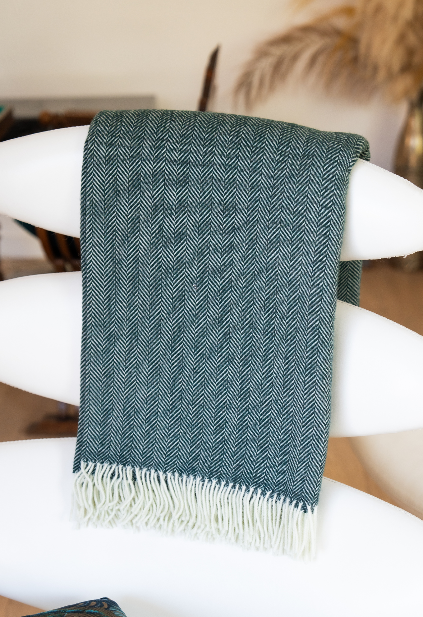 Plaid vert à chevrons sur un fauteuil blanc. Le plaid est enroulé autour du dossier et présente des franges blanches.