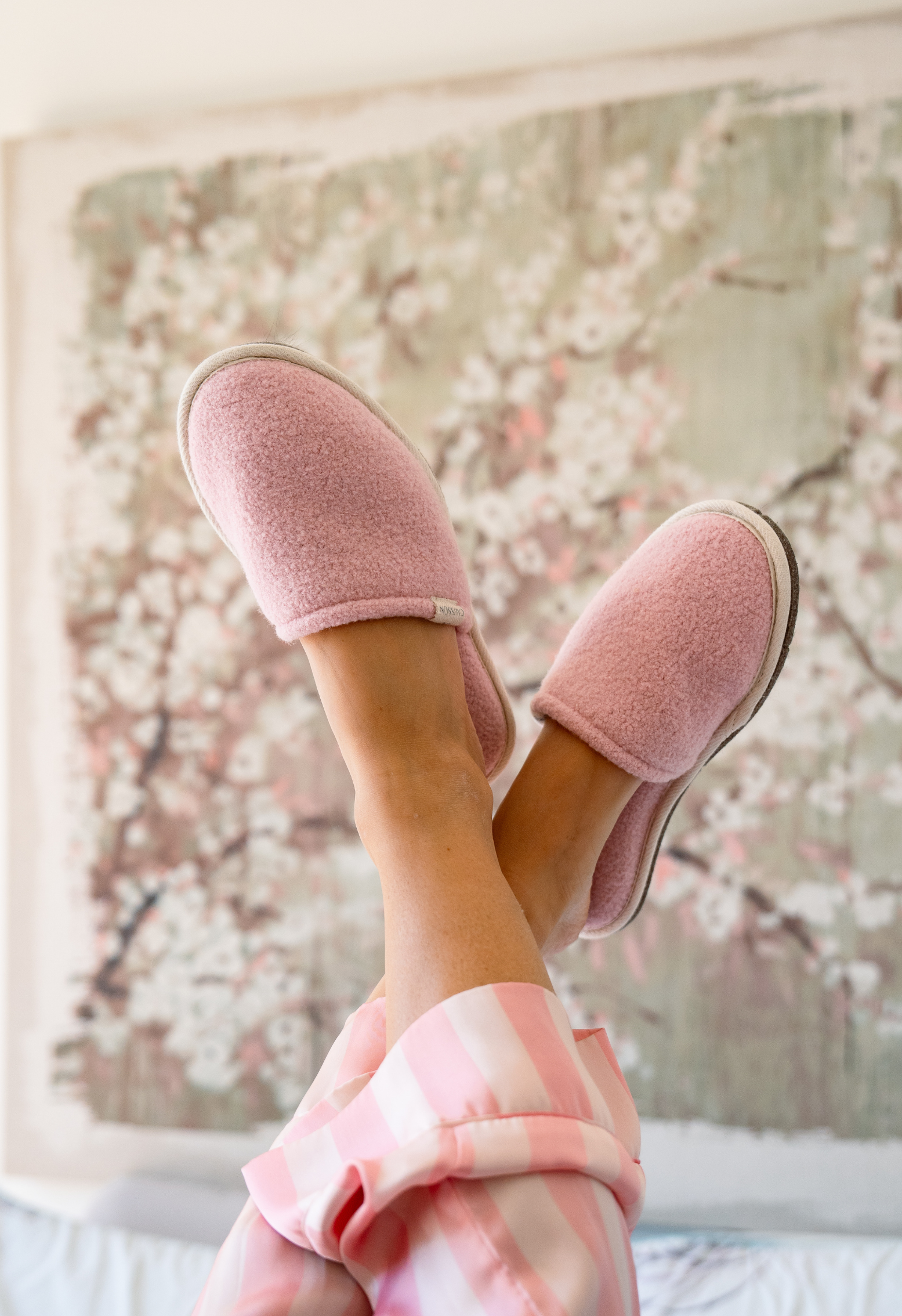 Gros plan des pieds croisés en pantoufles roses à poils sur fond de peinture floue. Les pieds portent un pyjama rose à rayures.