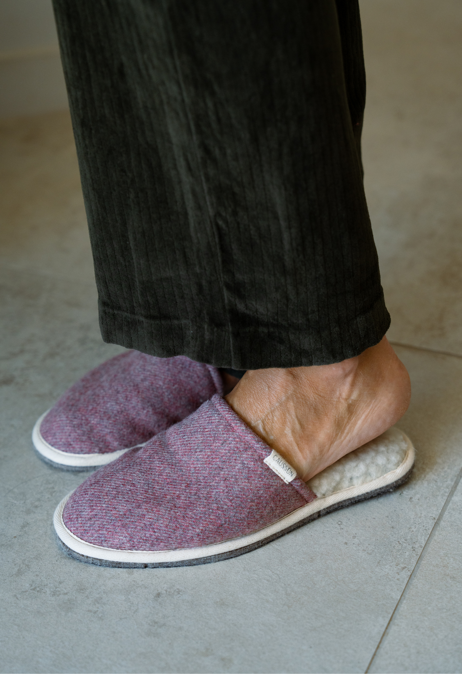 Pieds portant des chaussons roses et des pantalons verts en velours côtelé, sur un sol carrelé.