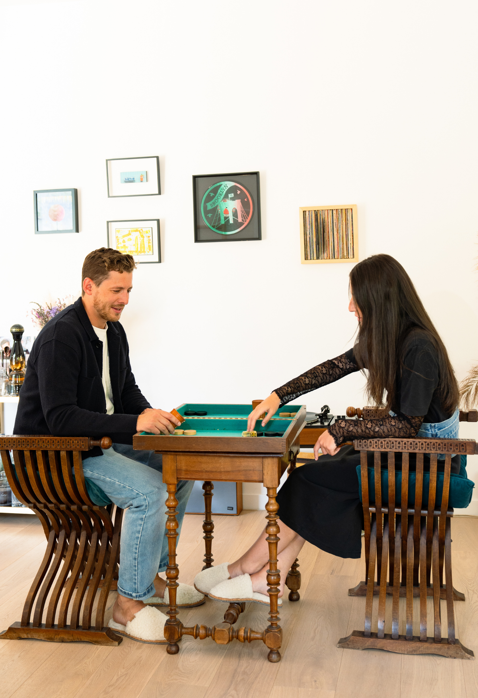 Couple joue à un jeu de société sur une table en bois, assis dans des chaises en bois incurvées, dans un intérieur chaleureux.