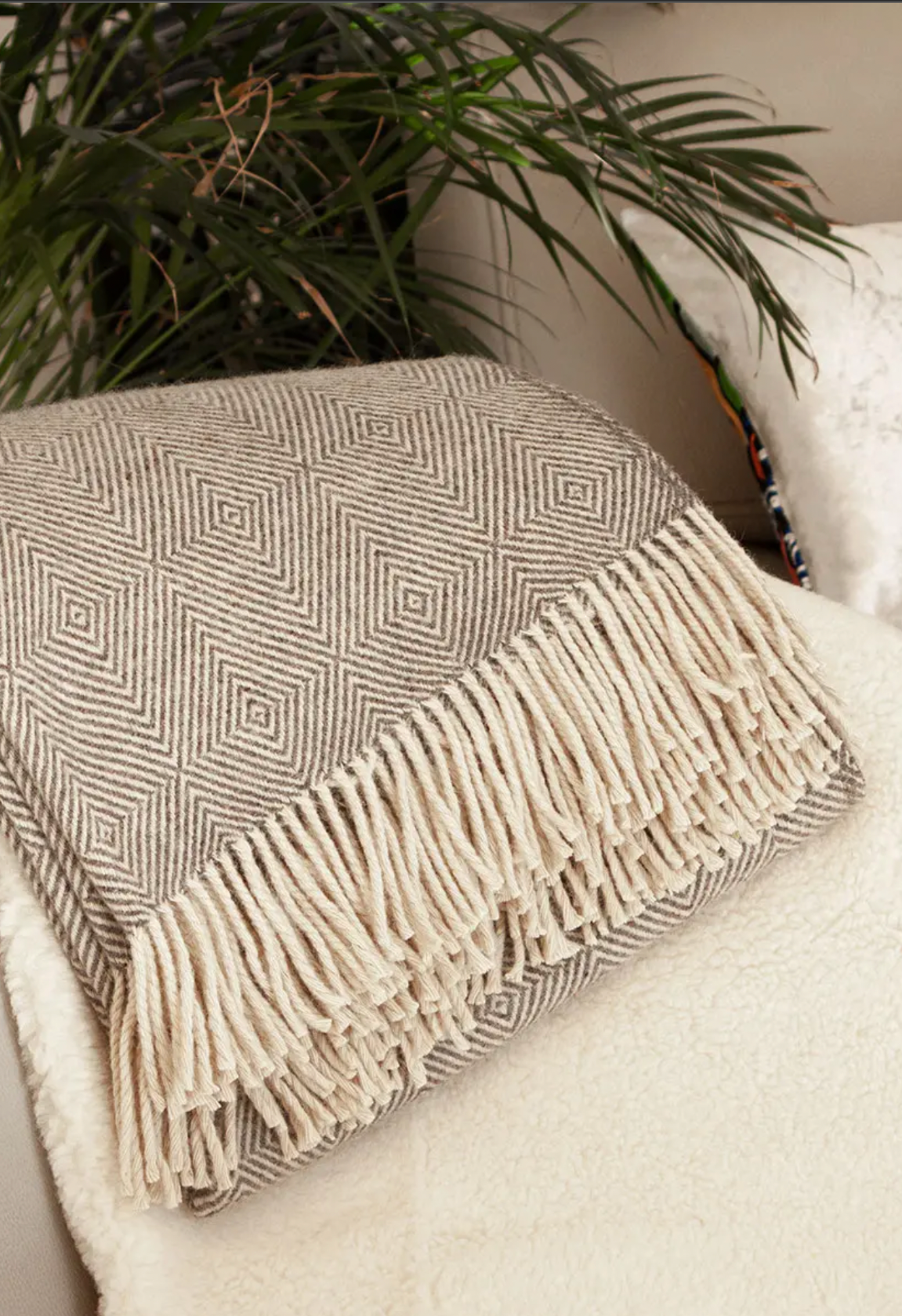 Plaid en laine à motifs géométriques et franges, posé sur un coussin moelleux. Un peu de verdure en arrière-plan.