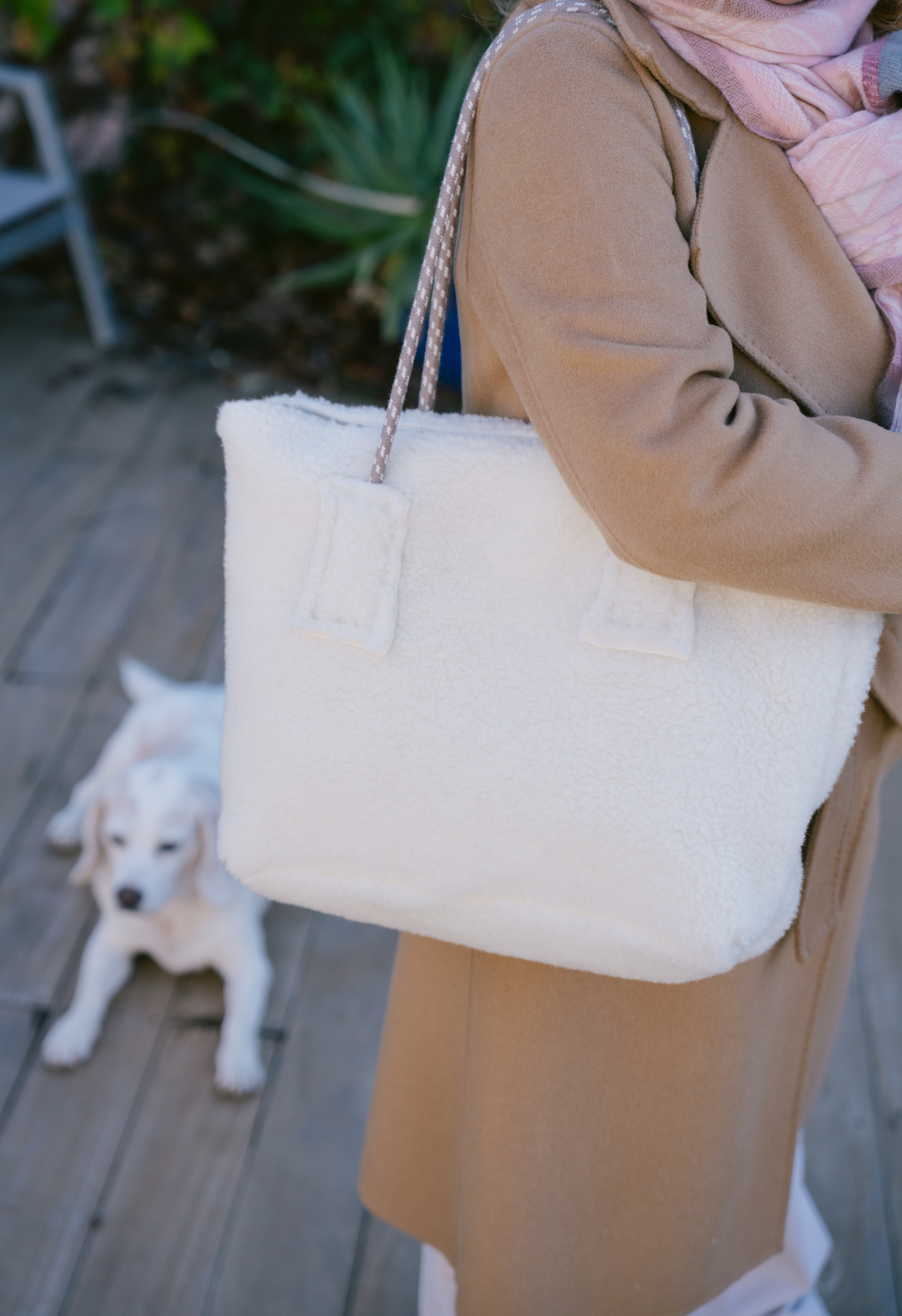 Femme portant un sac en fausse fourrure blanche avec un chiot assis à l'arrière-plan.