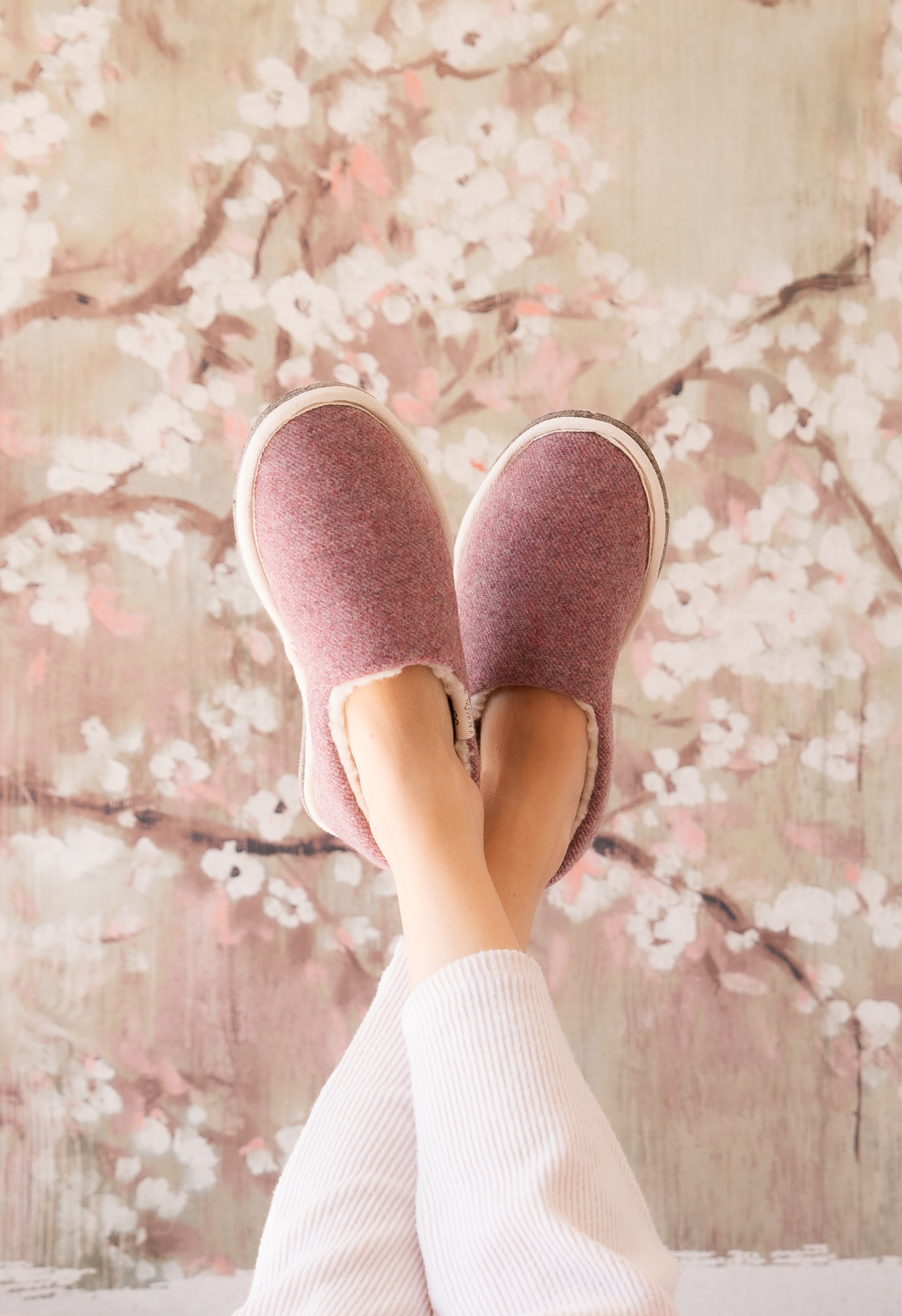 Pieds en pantoufles, les jambes croisées, devant un mur avec des fleurs. Bien-être et confort dans un cadre printanier.