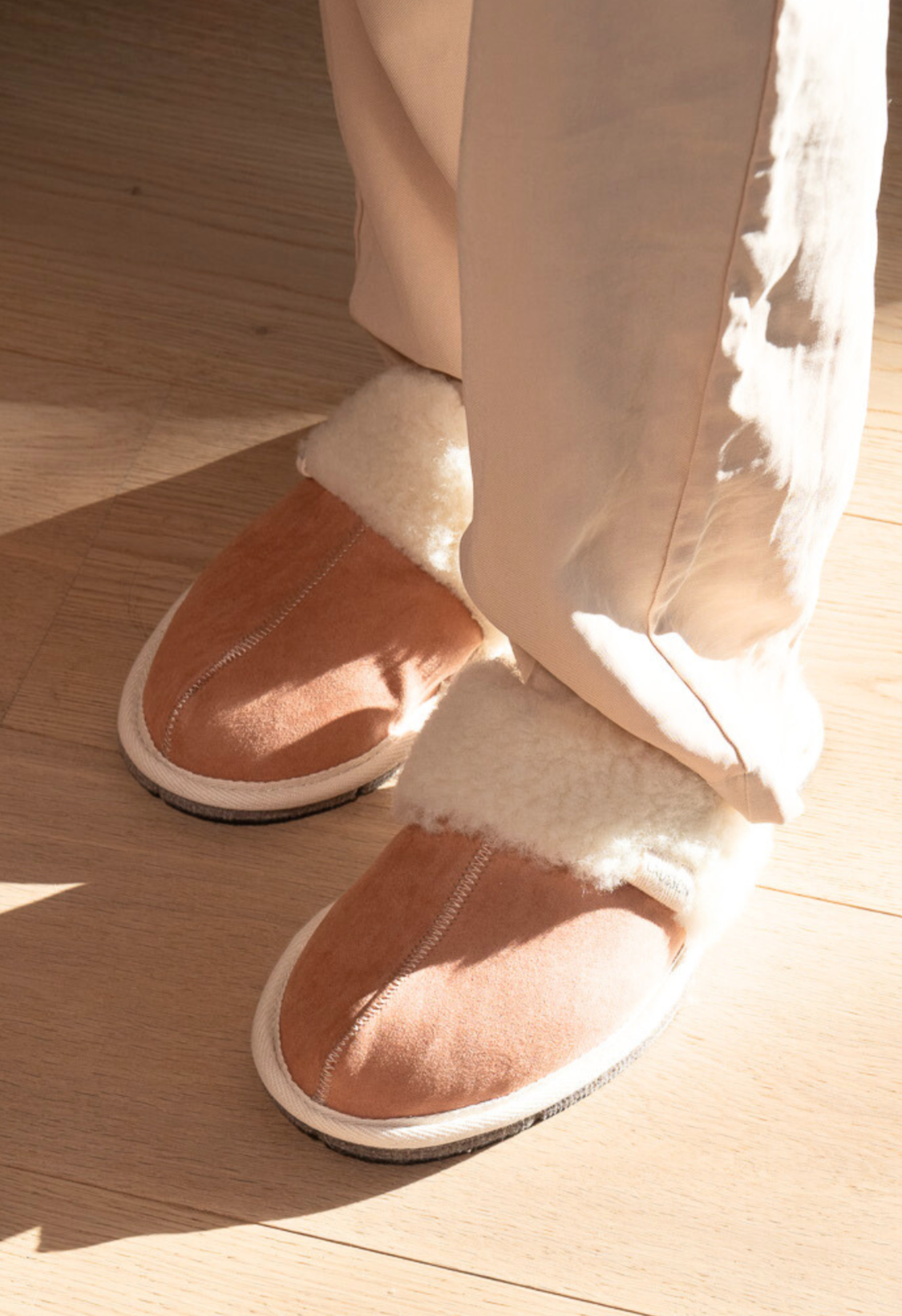 Pieds avec des pantoufles en peau de mouton confortables, vêtements de détente. Cadeaux de Noël et boules de Noël sont autour. Lumière naturelle.