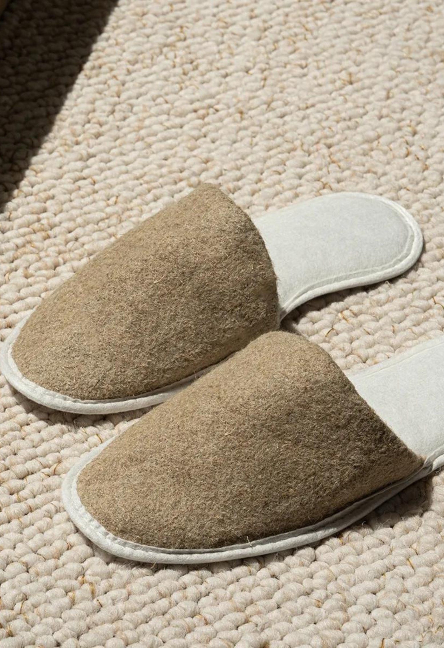 Une paire de pantoufles en laine de couleur beige sur un tapis en laine crème, lumière du soleil.