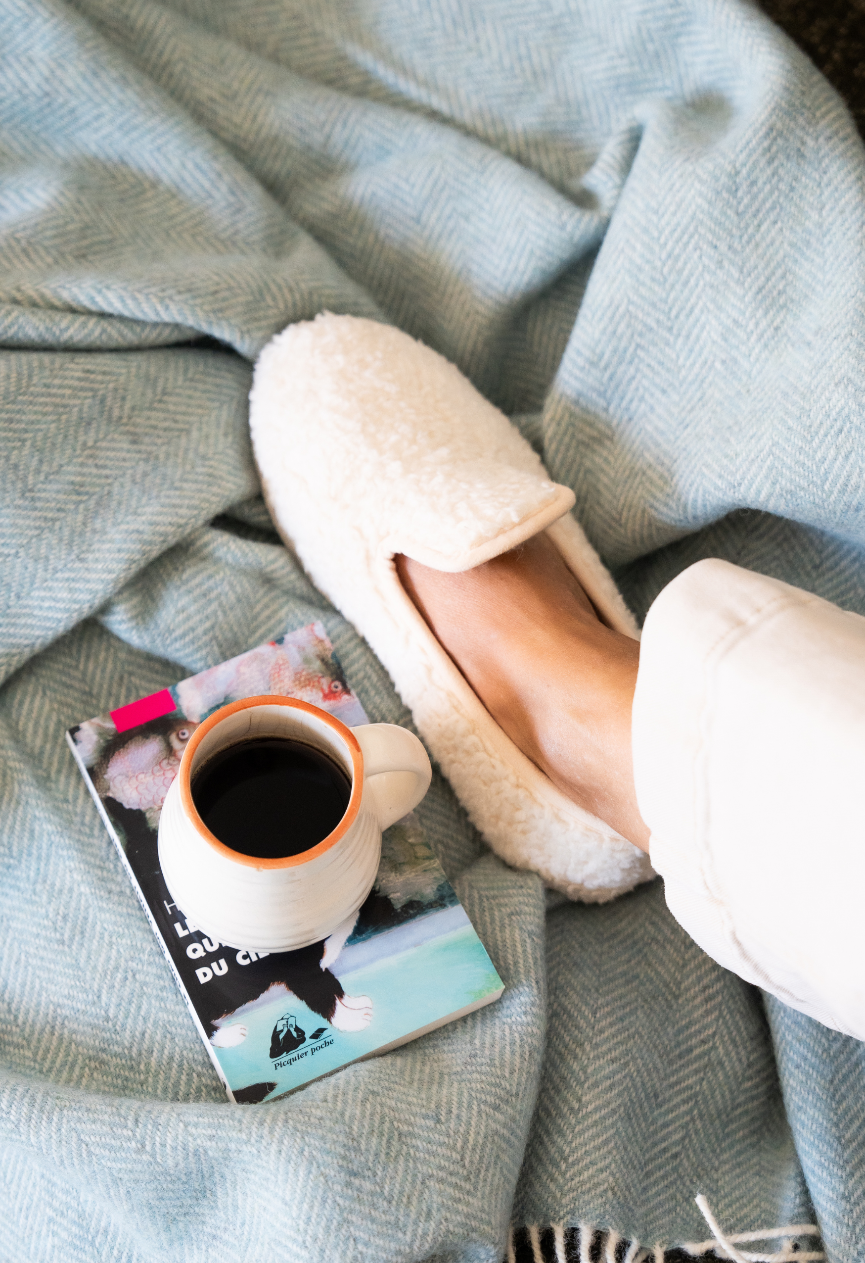 Pieds en pantoufles de laine sur une couverture en laine avec tasse de café et livre. Détente et confort à la maison.