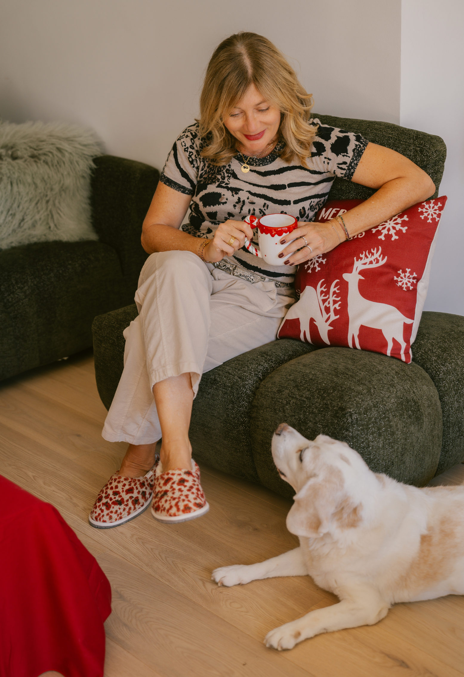 Une femme assise dans un fauteuil, avec une tasse de café et un chien blanc sur le sol. Décoration de Noël.