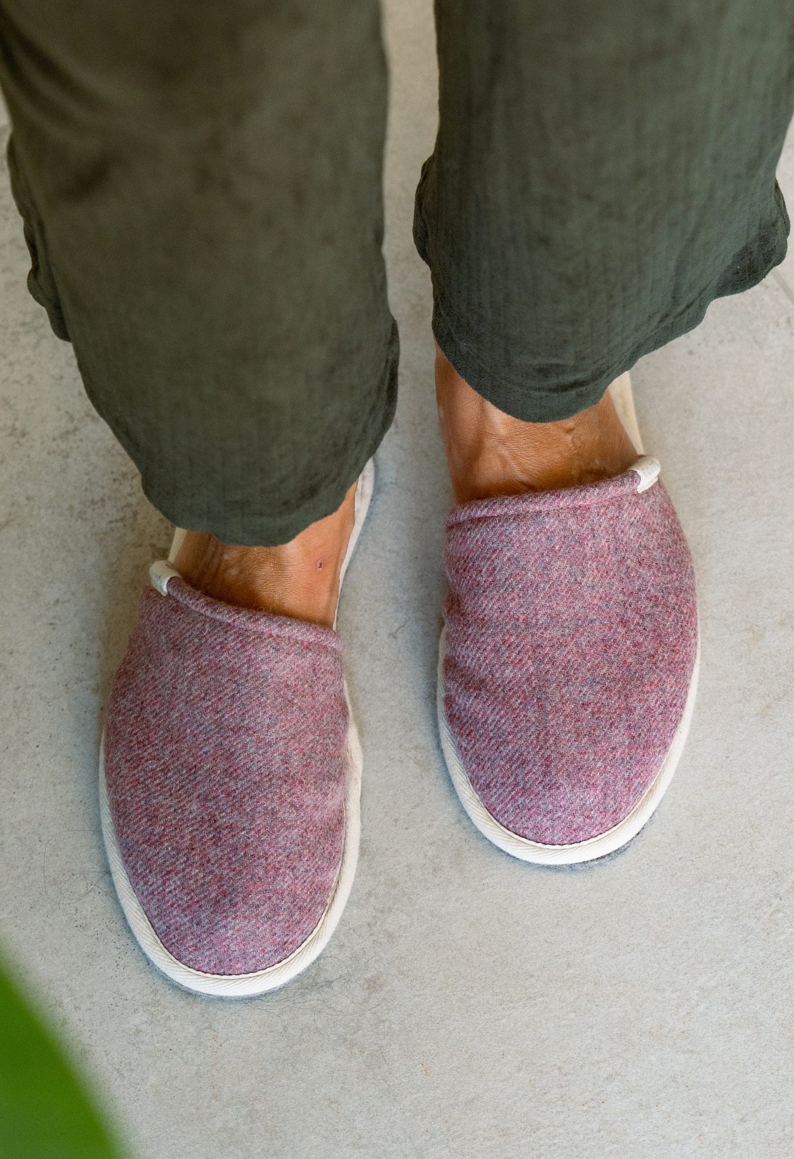 Gros plan des pieds d'une personne portant des pantoufles en laine rouge et un pantalon vert sur un sol gris.