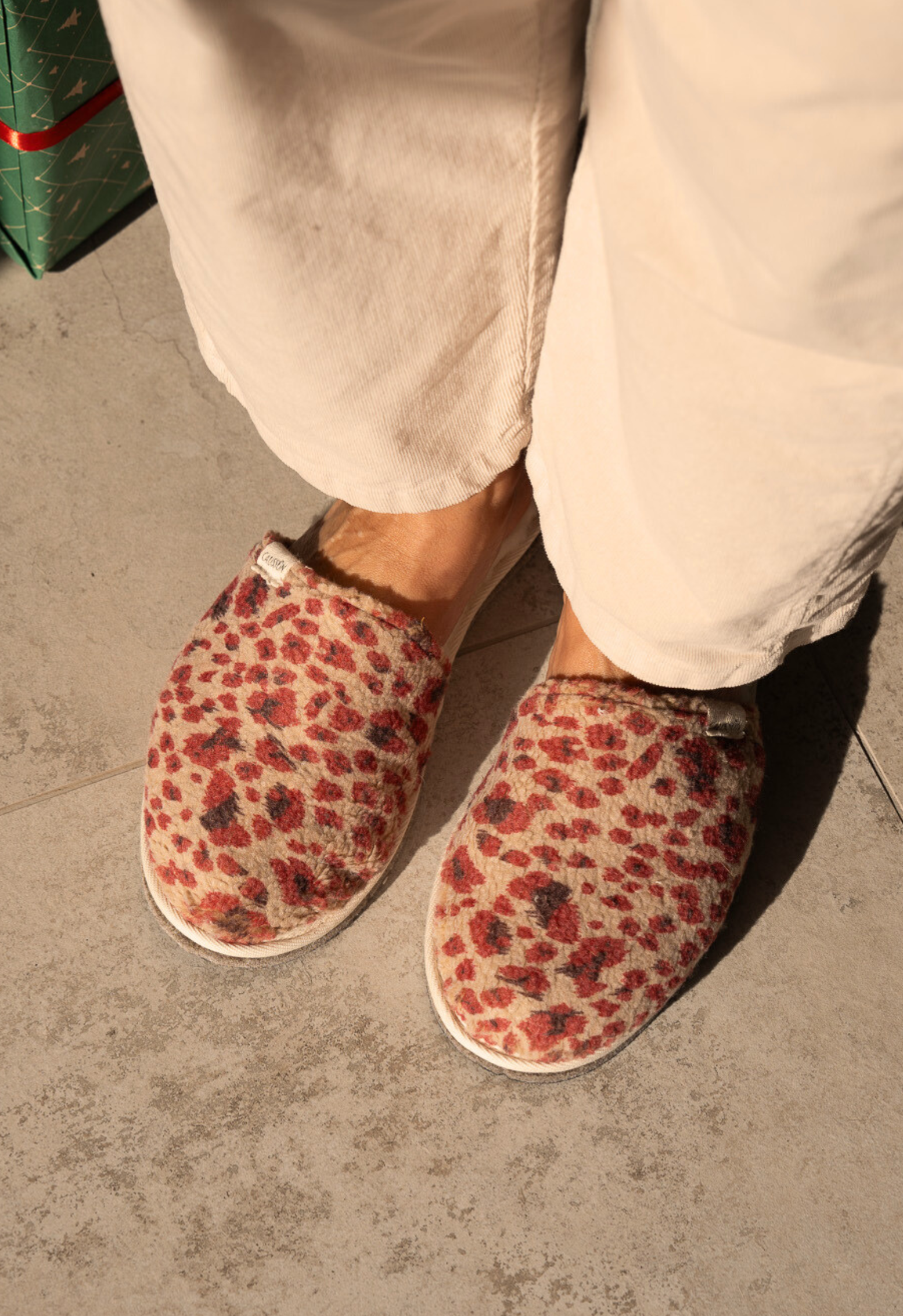 Une personne portant des chaussons léopard dans sa maison, près d'un cadeau emballé.